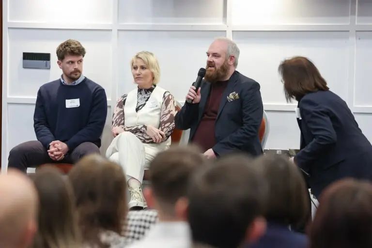 Panel at event with man holding and speaking into microphone