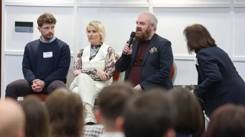 Panel at event with man holding and speaking into microphone